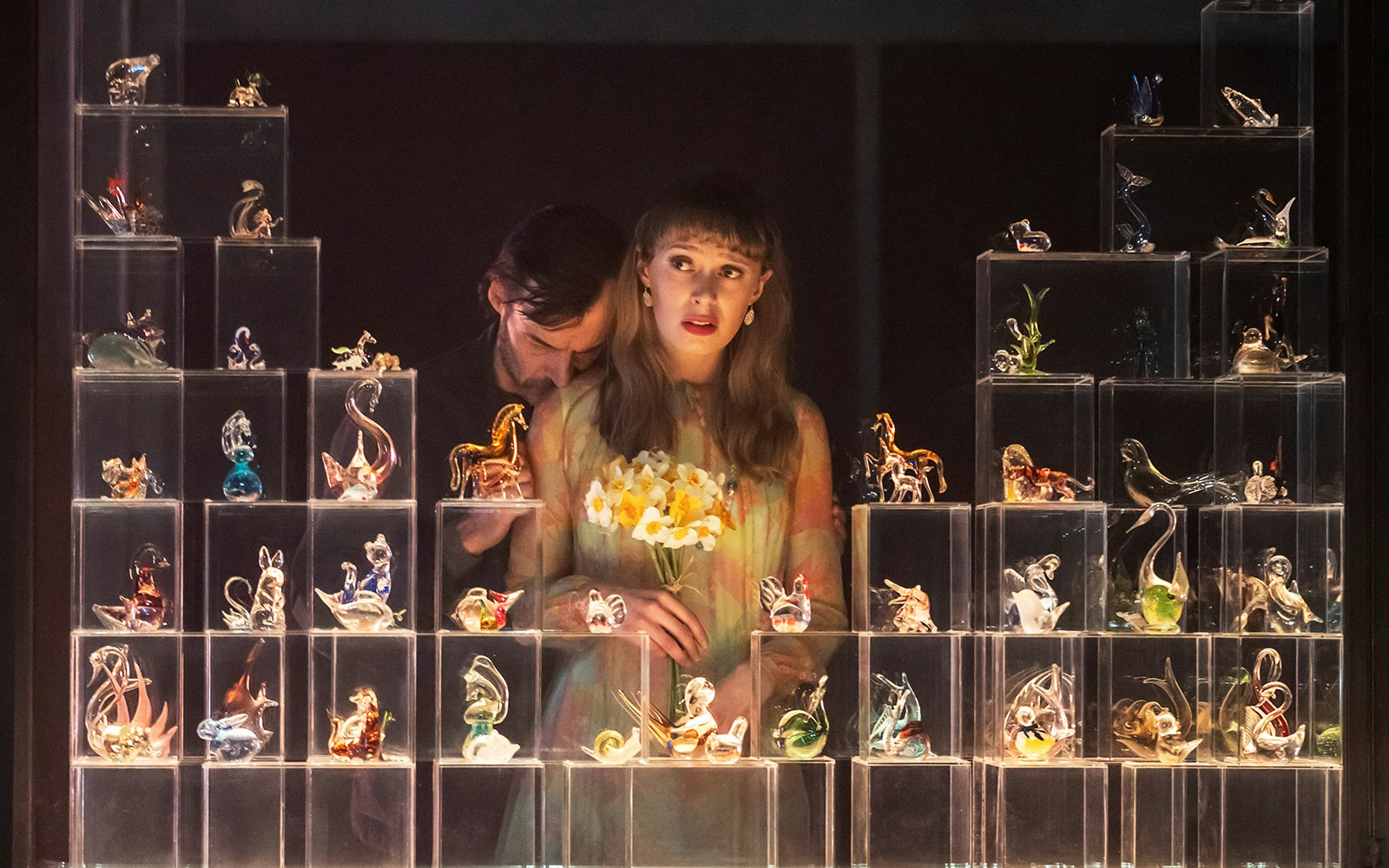 Glass figurines display with two people, one holding flowers, in "The Glass Menagerie" setting.