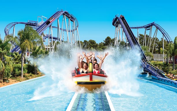 Visitors enjoying a water ride at Aquashow Water Park with roller coasters in the background.
