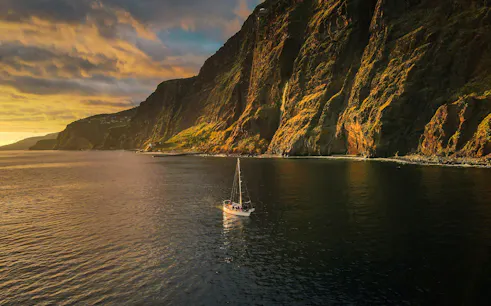 Sailboat on Madeira coast at sunset during dolphin and whale watching tour.