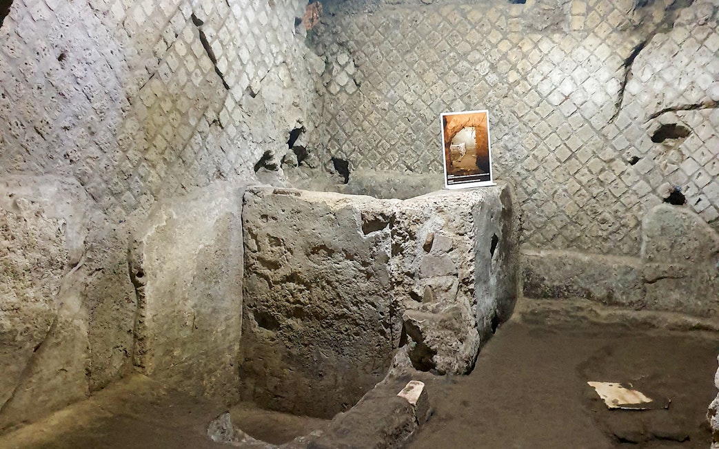Underground ruins in Naples with ancient stone walls and an informational sign.
