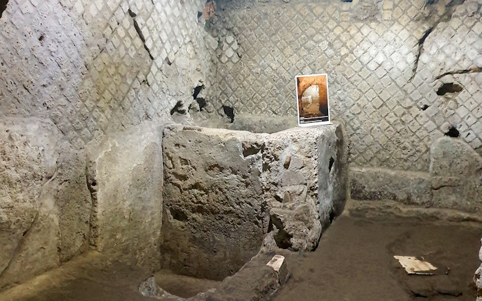 Underground ruins in Naples with ancient stone walls and an informational sign.