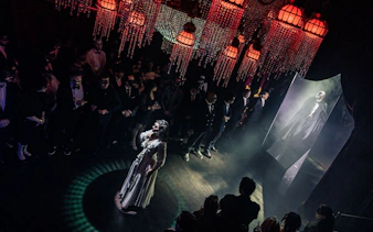 Masquerade Broadway stage performance with actors in masks and elegant costumes under chandeliers.