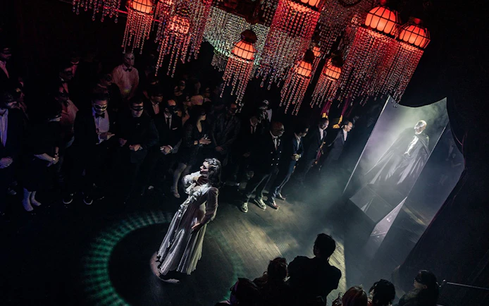 Masquerade Broadway stage performance with actors in masks and elegant costumes under chandeliers.