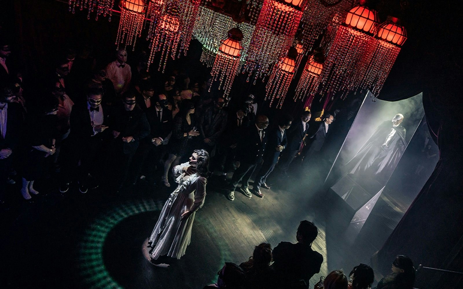 Masquerade Broadway stage performance with actors in masks and elegant costumes under chandeliers.