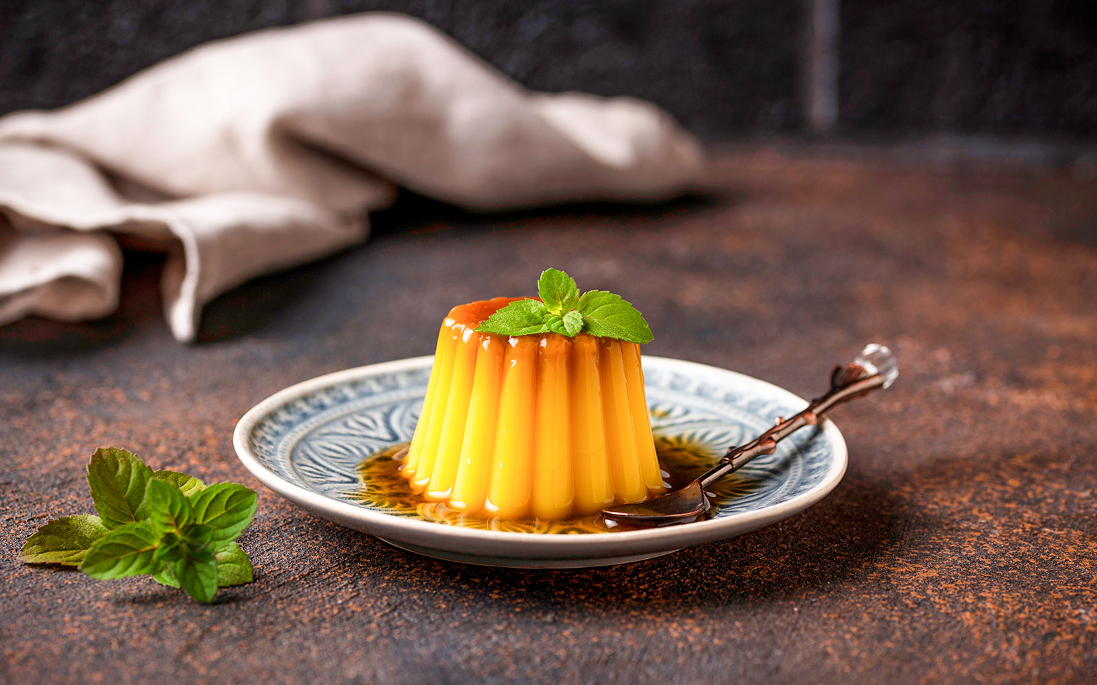 Flan dessert with caramel sauce and mint garnish on a decorative plate.