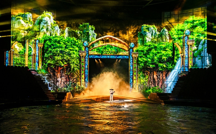 Performer on stage with water and lush forest backdrop during House of Dancing Water show.