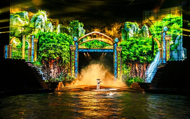 Performer on stage with water and lush forest backdrop during House of Dancing Water show.