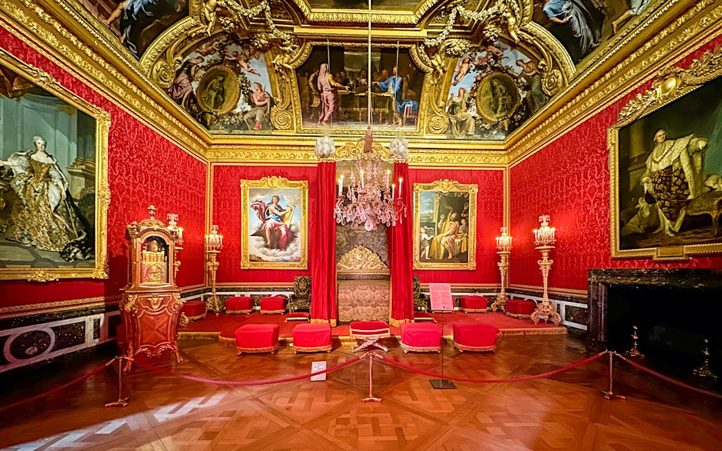 Royal Quarters interior at Palace of Versailles with ornate red and gold decor, chandeliers, and paintings.