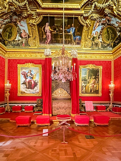Royal Quarters interior at Palace of Versailles with ornate red and gold decor, chandeliers, and paintings.