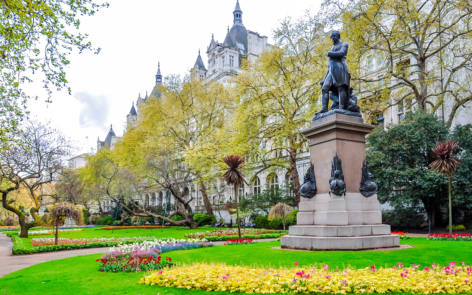 Statue in Victoria Embankment Gardens surrounded by spring flowers, London, UK.
