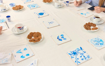 Guests painting traditional Dutch blue tiles at a workshop, with tea and stroopwafels on the table.