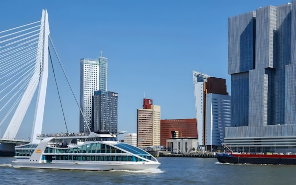 Cruise ship passing Erasmus Bridge and modern skyline in Rotterdam Harbor.