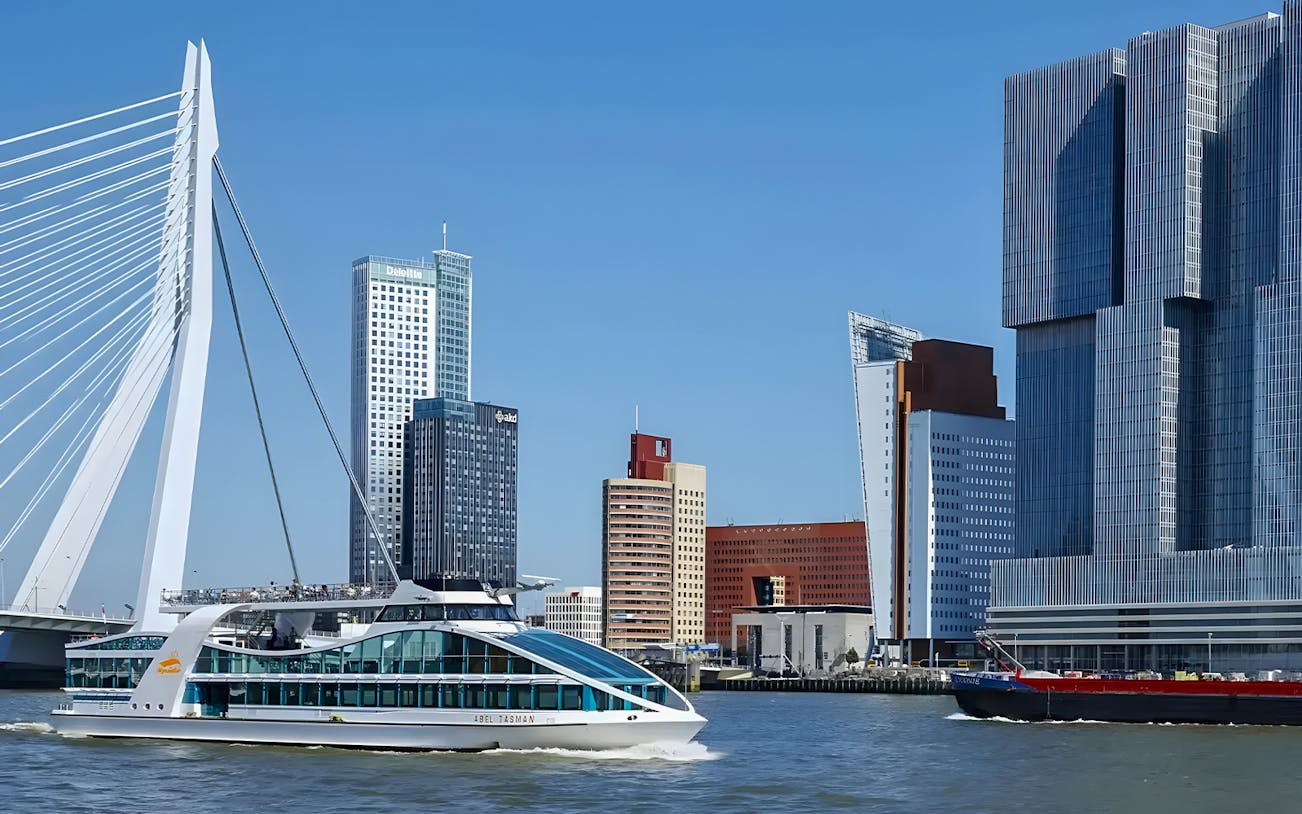 Cruise ship passing Erasmus Bridge and modern skyline in Rotterdam Harbor.