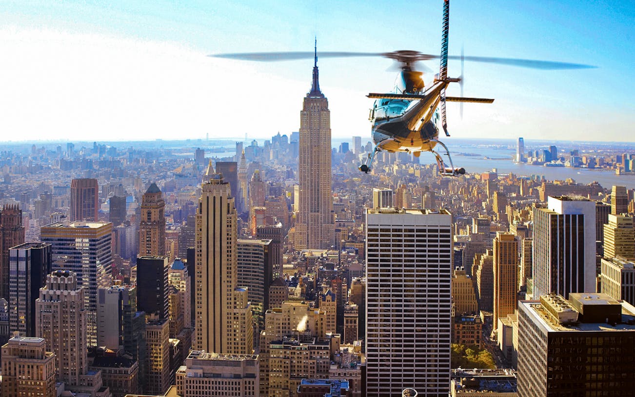 Helicopter flying over New York City skyline with Empire State Building in view.