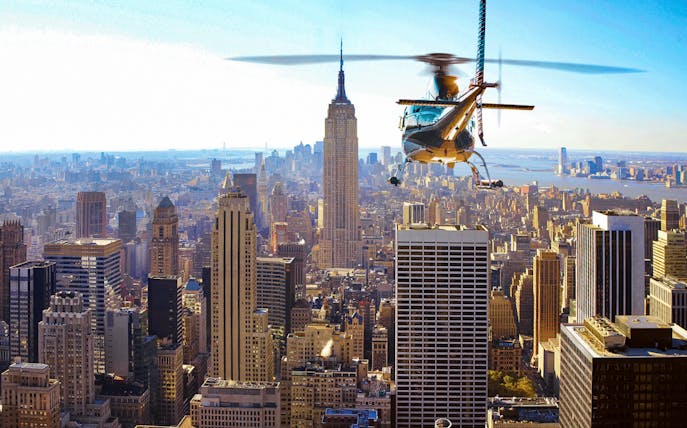 Helicopter flying over New York City skyline with Empire State Building in view.