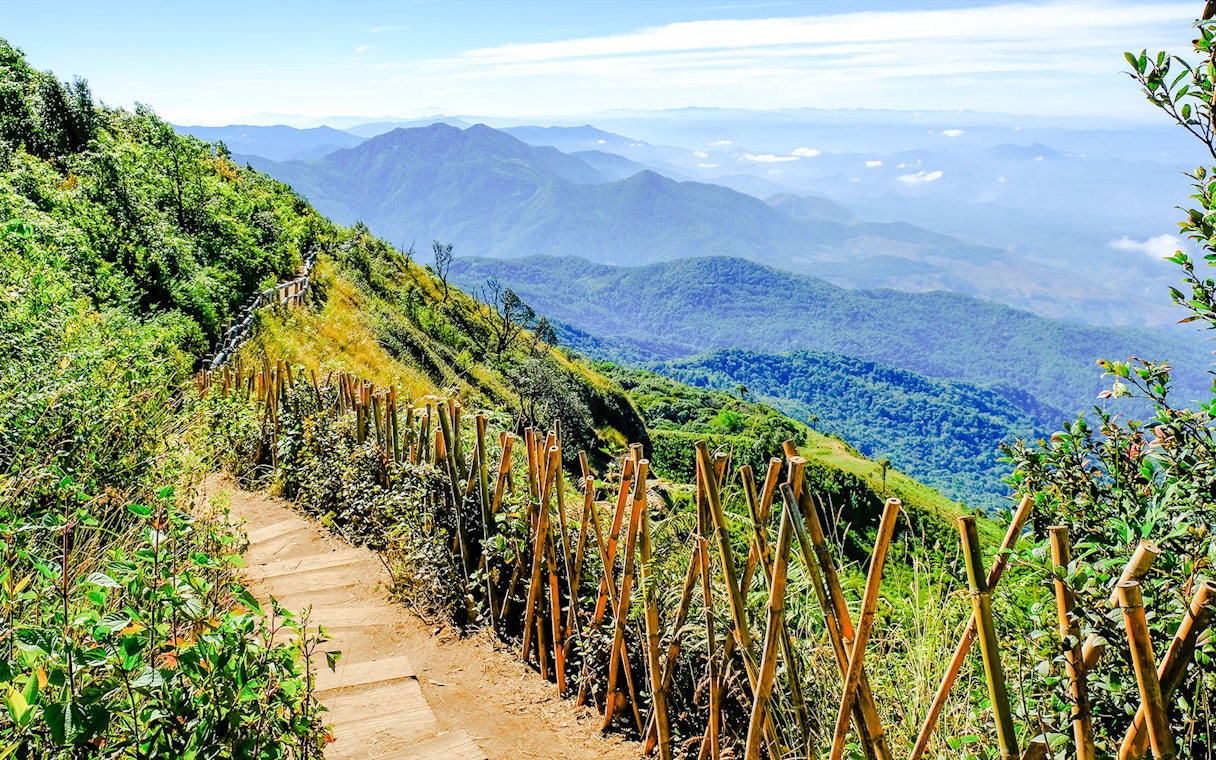 Nature trail with wooden fence on Doi Inthanon, Chiangmai, Thailand, overlooking lush mountains.