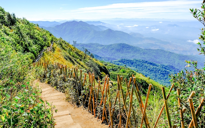 Nature trail with wooden fence on Doi Inthanon, Chiangmai, Thailand, overlooking lush mountains.