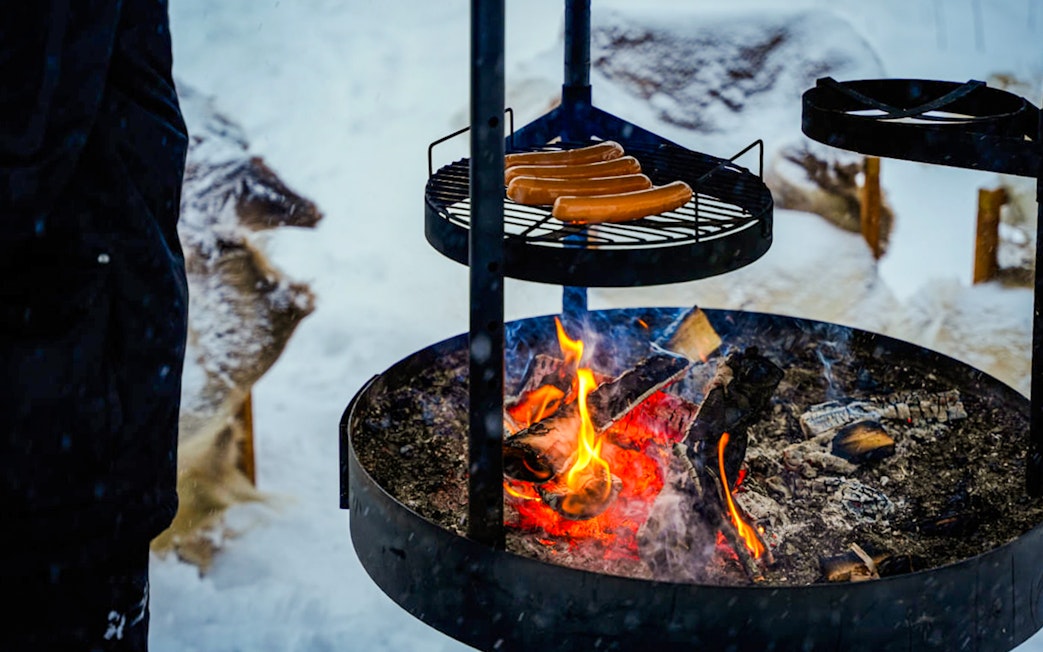 Grilling sausages over an open fire during Arctic Snowmobile Safari in Rovaniemi.