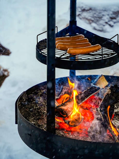 Grilling sausages over an open fire during Arctic Snowmobile Safari in Rovaniemi.