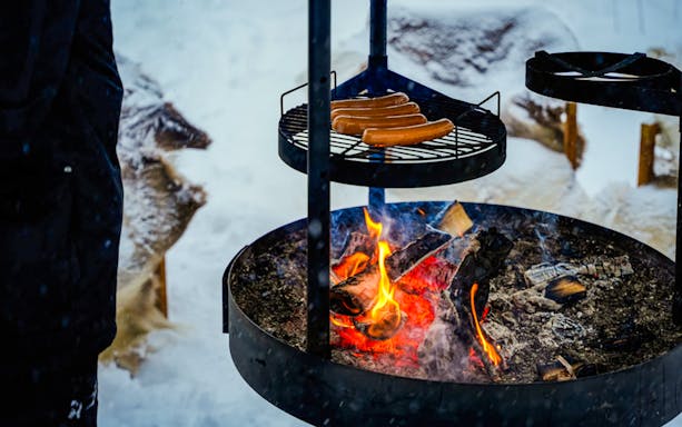 Grilling sausages over an open fire during Arctic Snowmobile Safari in Rovaniemi.