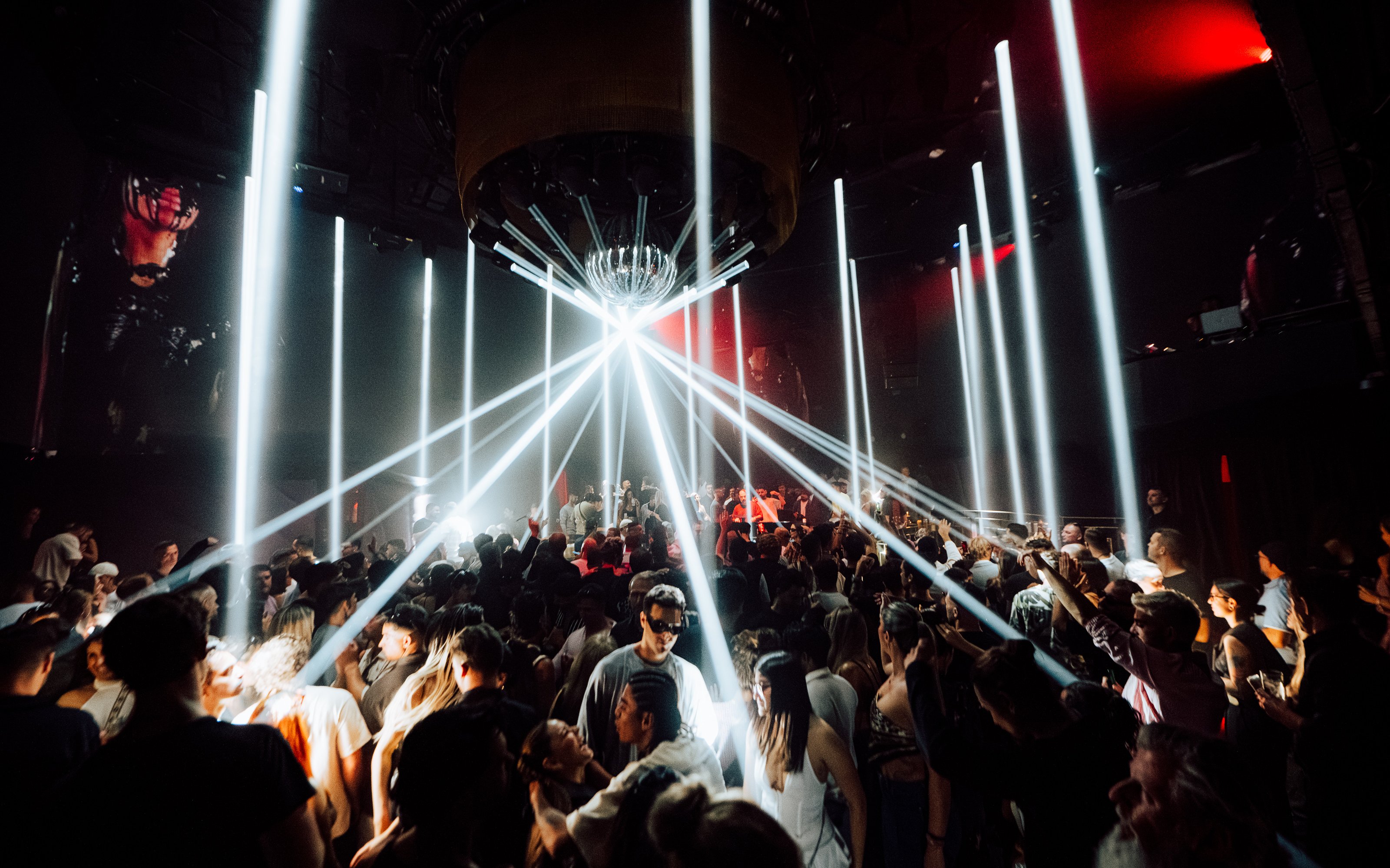DJ performing at La Troya Club Chinois, Ibiza with vibrant crowd and light beams.