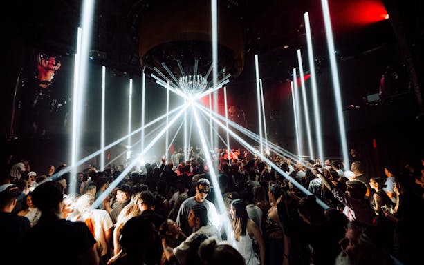DJ performing at La Troya Club Chinois, Ibiza with vibrant crowd and light beams.