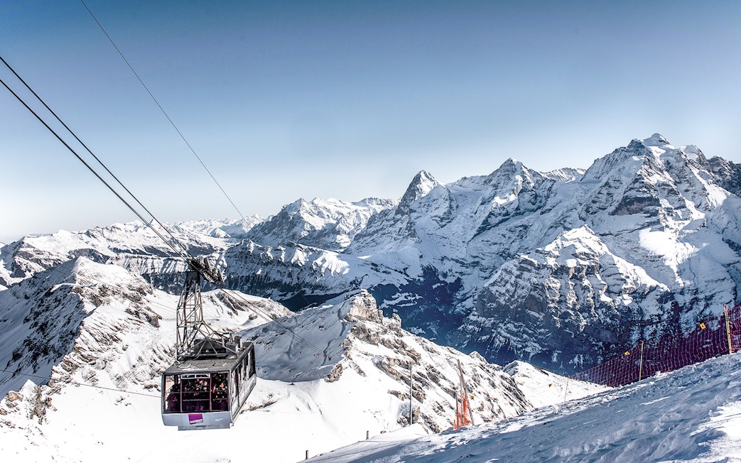 Cable car ascending to Schilthorn Piz Gloria with snowy Swiss Alps in the background.