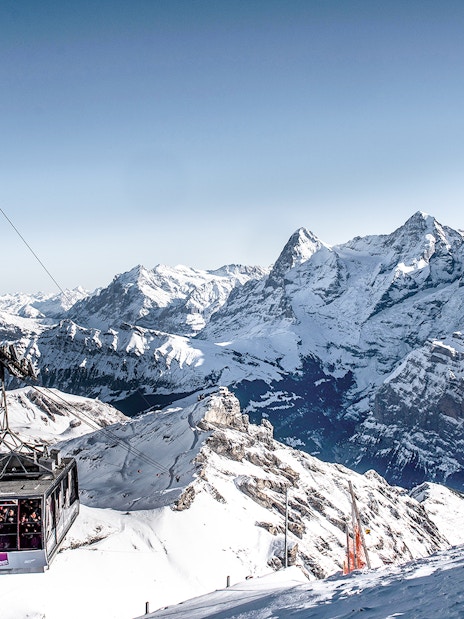 Cable car ascending to Schilthorn Piz Gloria with snowy Swiss Alps in the background.
