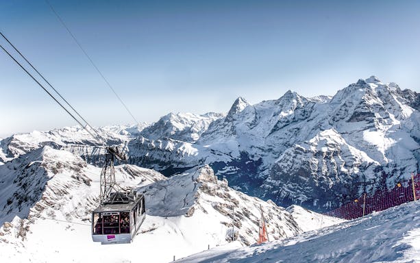 Cable car ascending to Schilthorn Piz Gloria with snowy Swiss Alps in the background.