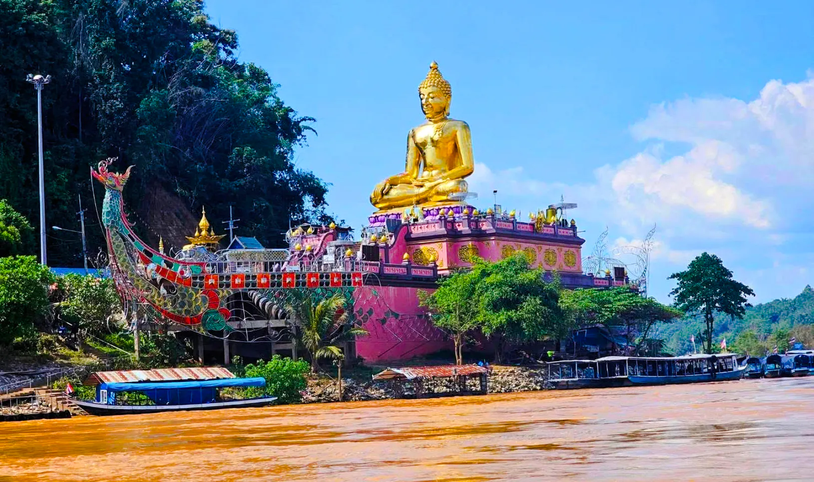 Golden Buddha statue at Golden Triangle, Chiang Rai, viewed from the river with boats nearby.