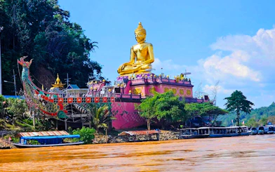 Golden Buddha statue at Golden Triangle, Chiang Rai, viewed from the river with boats nearby.