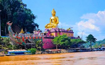 Golden Buddha statue at Golden Triangle, Chiang Rai, viewed from the river with boats nearby.