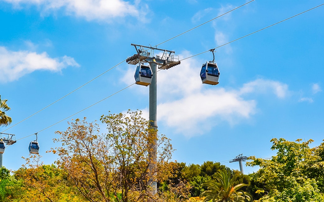 Cable cars ascending Montjuic hill in Barcelona, Spain, with trees below.