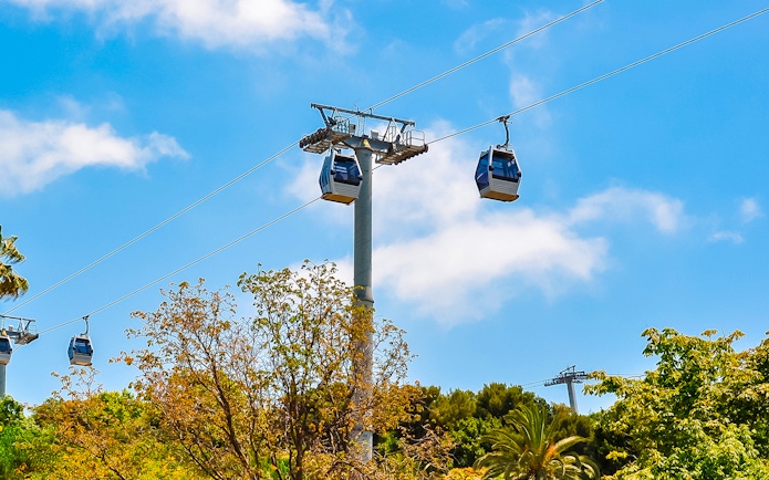 Cable cars ascending Montjuic hill in Barcelona, Spain, with trees below.