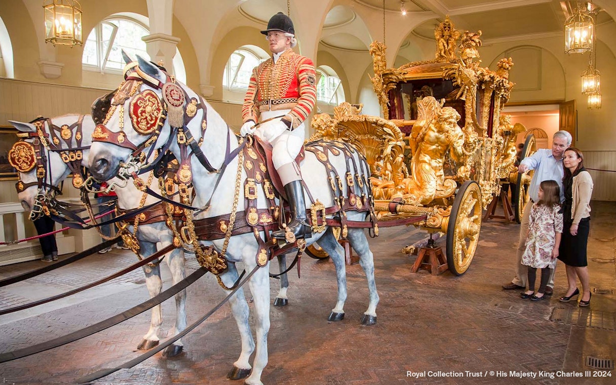 Royal carriage with ornate gold details and tourists observing at Buckingham Palace.
