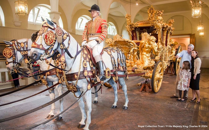 Royal carriage with ornate gold details and tourists observing at Buckingham Palace.