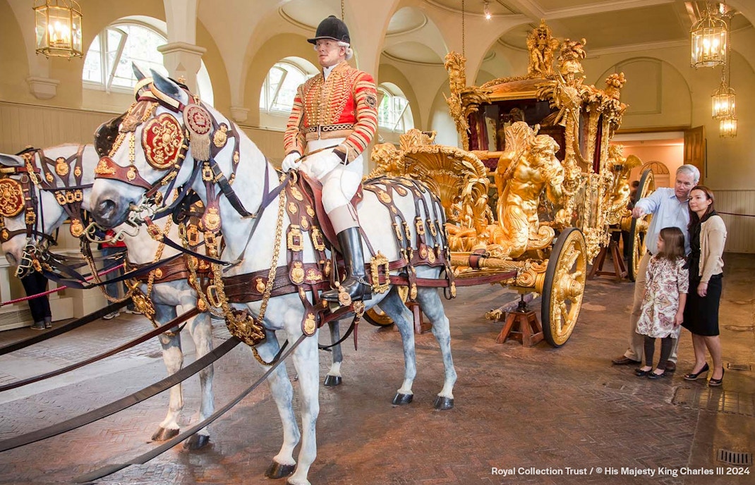 Royal carriage with ornate gold details and tourists observing at Buckingham Palace.