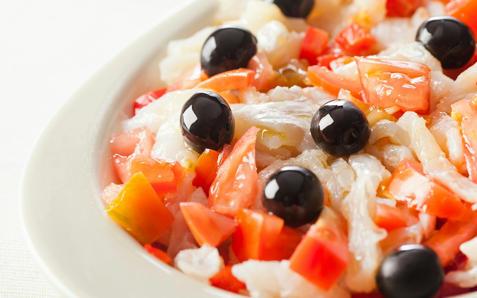 Esqueixada dish with cod, tomatoes, and black olives on a white plate.
