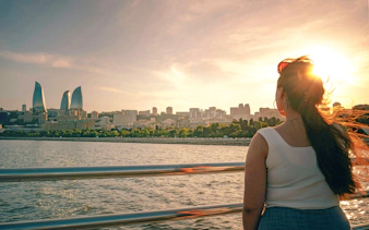 Woman on boat tour with view of Baku skyline and Flame Towers at sunset.