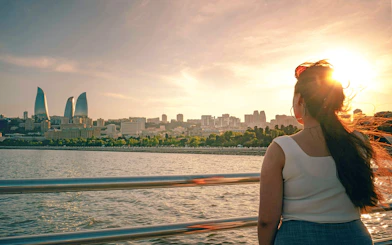 Woman on boat tour with view of Baku skyline and Flame Towers at sunset.
