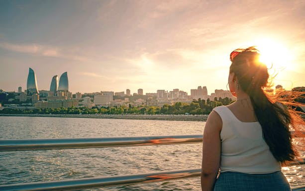 Woman on boat tour with view of Baku skyline and Flame Towers at sunset.