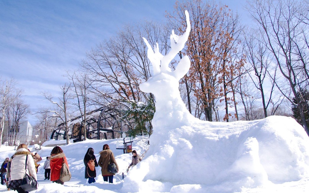 Snow sculpture of a deer at Asahiyama Zoo, Hokkaido, Japan, with visitors nearby.
