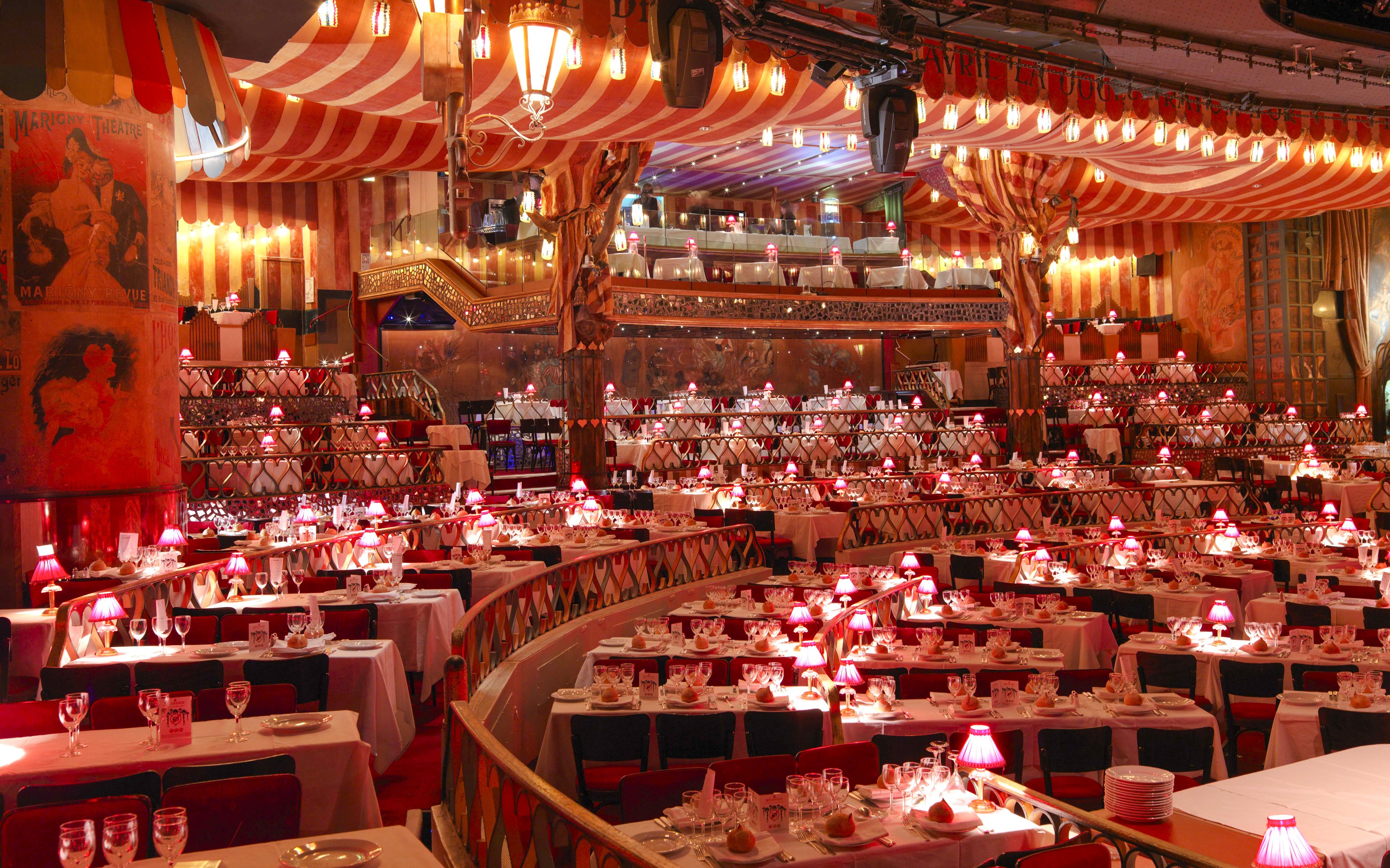 Dining setup at Moulin Rouge Show in Paris with red lamps and tiered seating.