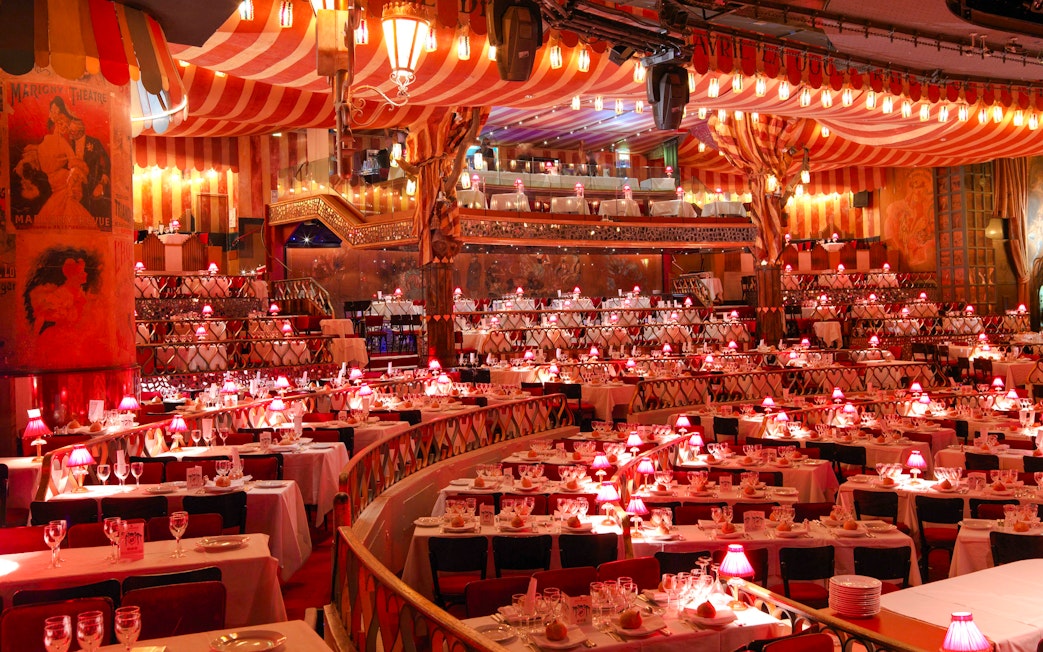 Dining setup at Moulin Rouge Show in Paris with red lamps and tiered seating.