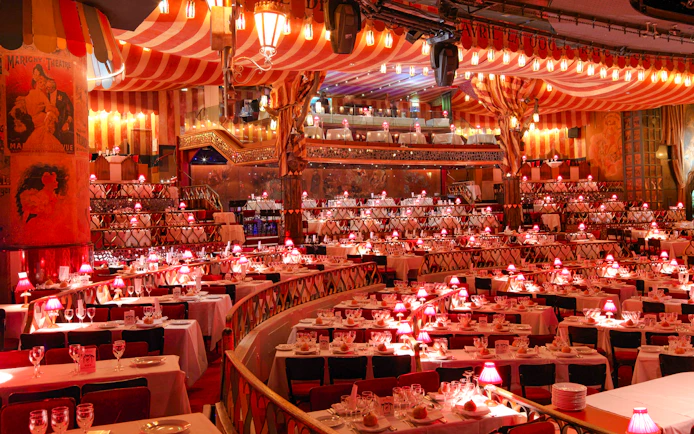 Dining setup at Moulin Rouge Show in Paris with red lamps and tiered seating.