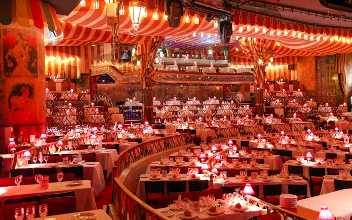 Dining setup at Moulin Rouge Show in Paris with red lamps and tiered seating.