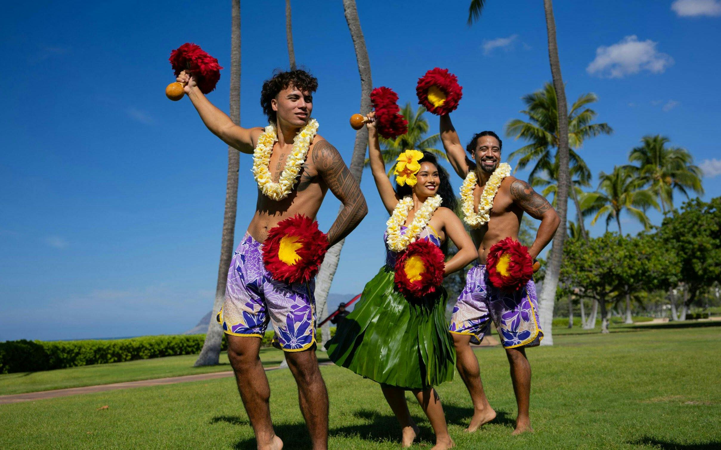 Performers at a Kaula-Luau in Hawaii, wearing traditional attire and holding feathered gourd rattles.