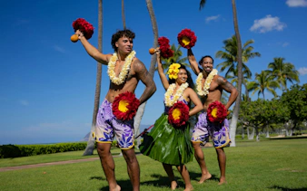 Performers at a Kaula-Luau in Hawaii, wearing traditional attire and holding feathered gourd rattles.