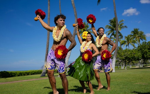 Performers at a Kaula-Luau in Hawaii, wearing traditional attire and holding feathered gourd rattles.