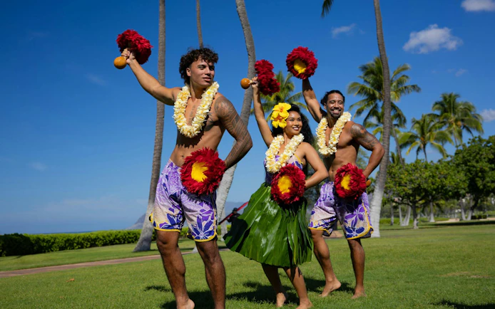 Performers at a Kaula-Luau in Hawaii, wearing traditional attire and holding feathered gourd rattles.